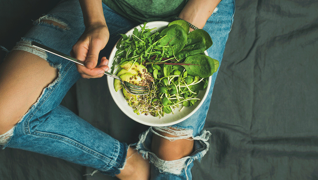 Pretty girl sitting on the floor eating a green salad